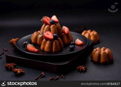 Delicious cupcakes or muffins with raisins and nuts, strawberries and blueberries on a ceramic plate on a textured concrete table