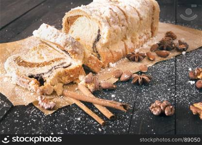 Delicious dessert on baking paper, a sponge cake filled with poppy seeds and roasted walnuts and almonds, covered with powdered sugar, on a black wooden table
