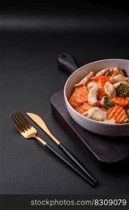 Delicious dish consisting of pieces of boiled chicken, broccoli and carrots with spices and herbs on a dark concrete background