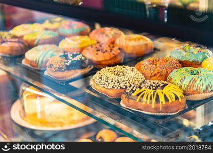 Delicious donuts decorated with different decorations displayed in cafe glass cabinet. Selective focus blured background