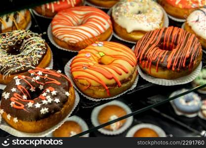 Delicious donuts decorated with different decorations displayed in cafe glass cabinet. Selective focus blured background
