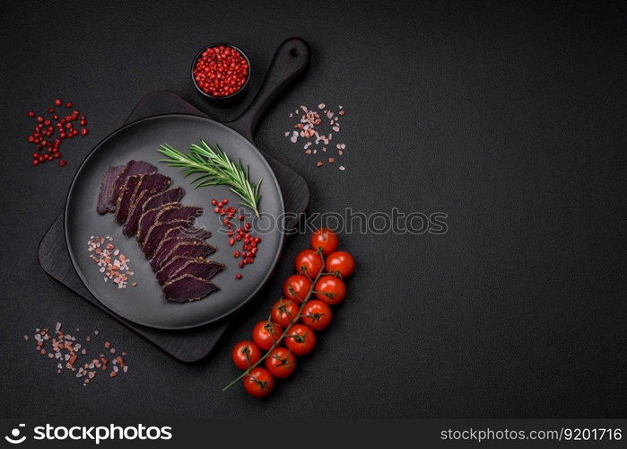 Delicious dried smoked beef or horse meat jerky with spices and salt on a dark concrete background