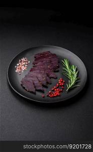 Delicious dried smoked beef or horse meat jerky with spices and salt on a dark concrete background