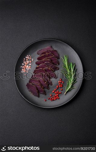 Delicious dried smoked beef or horse meat jerky with spices and salt on a dark concrete background