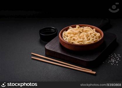 Delicious dried squid in the form of shavings with salt and spices on a ceramic plate on a dark concrete background