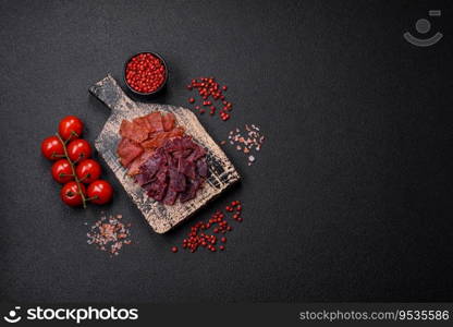 Delicious dried veal or turkey jerky with salt, spices and herbs on a dark concrete background