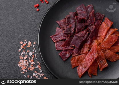 Delicious dried veal or turkey jerky with salt, spices and herbs on a dark concrete background