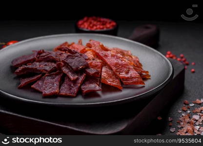 Delicious dried veal or turkey jerky with salt, spices and herbs on a dark concrete background