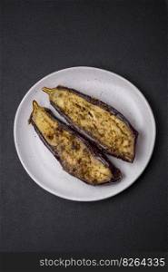 Delicious eggplant cut into two halves baked with salt, spices and herbs on a dark concrete background