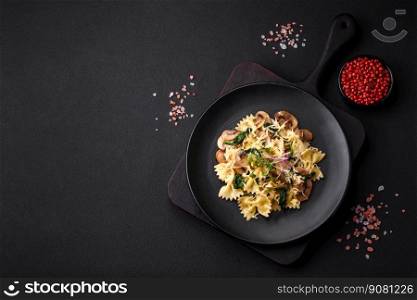 Delicious farfalle pasta with mushrooms, cheese and spinach with spices on a black plate on a dark concrete background