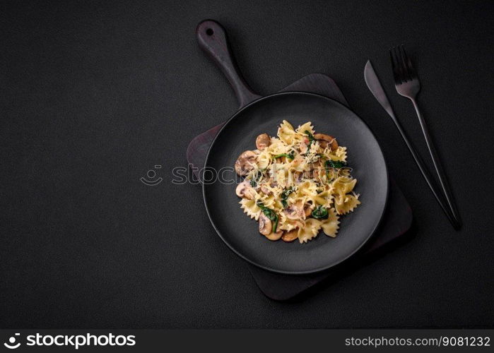 Delicious farfalle pasta with mushrooms, cheese and spinach with spices on a black plate on a dark concrete background