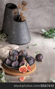 Delicious figs in a plate. Kitchrn countertop decorated with modern design black ceramic vases with ornamental dry natural plants . Space for text
