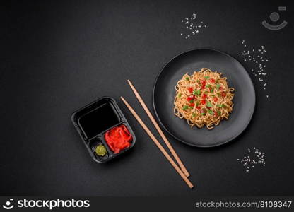 Delicious fresh Asian noodles with vegetables, salt, spices and herbs on a ceramic plate on a dark concrete background