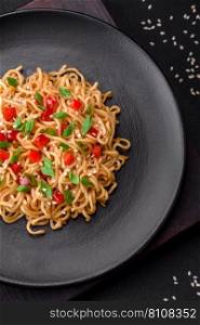 Delicious fresh Asian noodles with vegetables, salt, spices and herbs on a ceramic plate on a dark concrete background