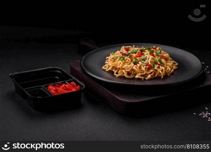 Delicious fresh Asian noodles with vegetables, salt, spices and herbs on a ceramic plate on a dark concrete background