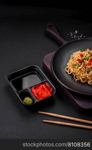 Delicious fresh Asian noodles with vegetables, salt, spices and herbs on a ceramic plate on a dark concrete background