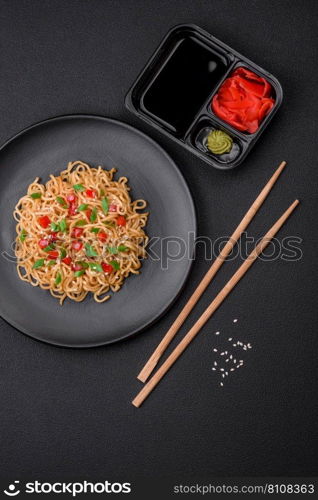 Delicious fresh Asian noodles with vegetables, salt, spices and herbs on a ceramic plate on a dark concrete background