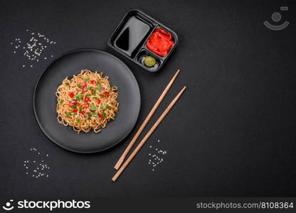 Delicious fresh Asian noodles with vegetables, salt, spices and herbs on a ceramic plate on a dark concrete background