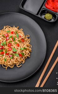 Delicious fresh Asian noodles with vegetables, salt, spices and herbs on a ceramic plate on a dark concrete background