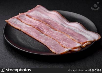 Delicious fresh bacon stripes with spices and salt on a dark concrete background