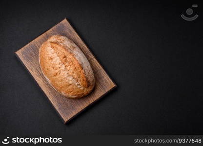 Delicious fresh baked crispy loaf of bread with seeds and grains on a dark concrete background