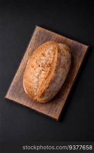 Delicious fresh baked crispy loaf of bread with seeds and grains on a dark concrete background