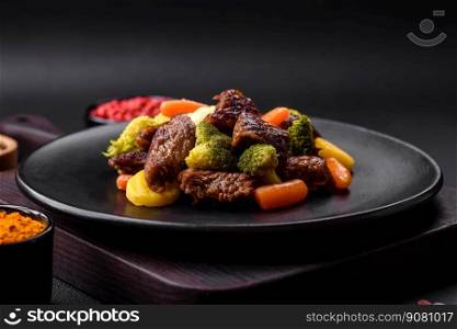 Delicious fresh beef and vegetables carrots, broccoli, cauliflower on a black plate on a dark concrete background