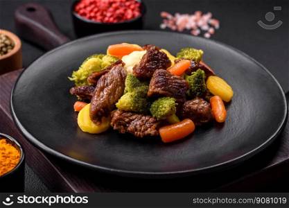 Delicious fresh beef and vegetables carrots, broccoli, cauliflower on a black plate on a dark concrete background