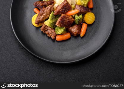 Delicious fresh beef and vegetables carrots, broccoli, cauliflower on a black plate on a dark concrete background