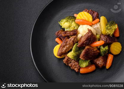 Delicious fresh beef and vegetables carrots, broccoli, cauliflower on a black plate on a dark concrete background