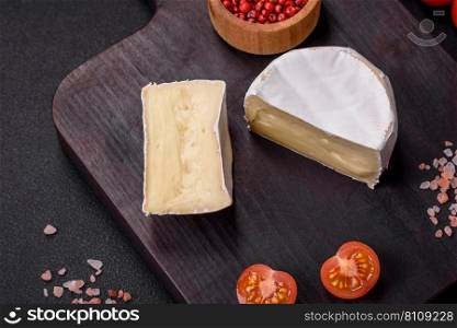 Delicious fresh brie cheese in the form of a mini head with cherry tomatoes on a dark concrete background