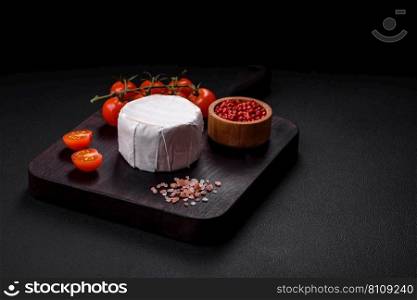 Delicious fresh brie cheese in the form of a mini head with cherry tomatoes on a dark concrete background