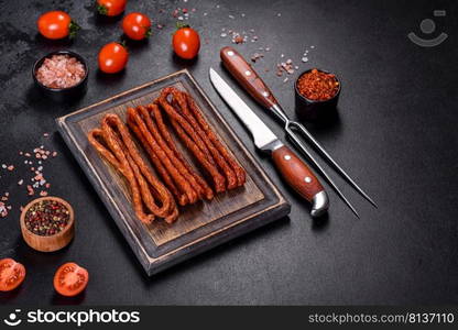 Delicious fresh bright smoked hot sausages with cherry tomatoes on a dark concrete table. Smoked hunting sausages on a black stone background. Top view. Free copy space