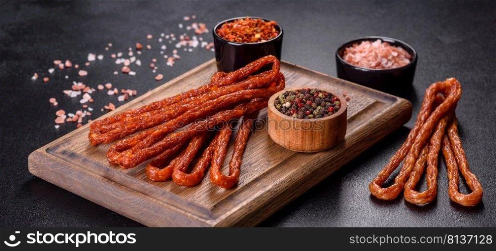 Delicious fresh bright smoked hot sausages with cherry tomatoes on a dark concrete table. Smoked hunting sausages on a black stone background. Top view. Free copy space