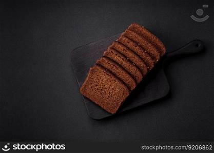 Delicious fresh brown bread with grains and seeds sliced on a wooden cutting board on a dark concrete background