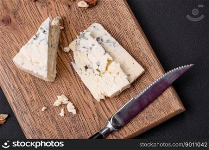 Delicious fresh cheese with blue mold dorblu on a wooden cutting board on a dark concrete background