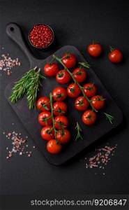 Delicious fresh cherry tomatoes on a twig with spices and herbs on a dark concrete background