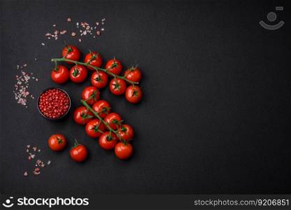 Delicious fresh cherry tomatoes on a twig with spices and herbs on a dark concrete background