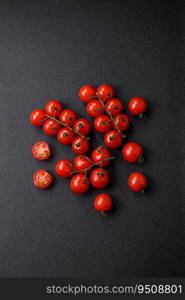 Delicious fresh cherry tomatoes on the branches as an ingredient for cooking a vegetarian dish on a dark concrete background