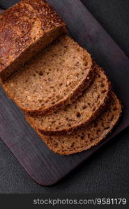 Delicious fresh crispy brown bread with grains and seeds on a dark concrete background