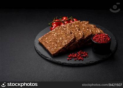 Delicious fresh crispy brown bread with seeds and grains cut into slices on a dark concrete background