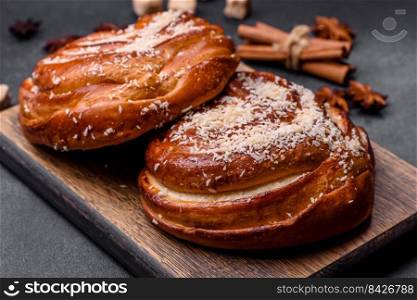 Delicious fresh crispy cinnamon buns sprinkled with coconut crumbs on a wooden cutting board against a dark concrete background. Delicious fresh crispy cinnamon buns sprinkled with coconut crumbs on a wooden cutting board
