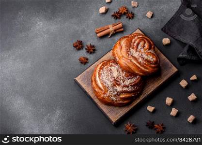 Delicious fresh crispy cinnamon buns sprinkled with coconut crumbs on a wooden cutting board against a dark concrete background. Delicious fresh crispy cinnamon buns sprinkled with coconut crumbs on a wooden cutting board