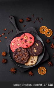 Delicious fresh crispy oatmeal cookies with chocolate and nuts on a black ceramic plate on a dark concrete background