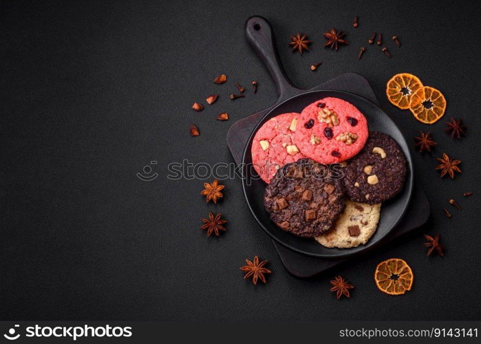 Delicious fresh crispy oatmeal cookies with chocolate and nuts on a black ceramic plate on a dark concrete background