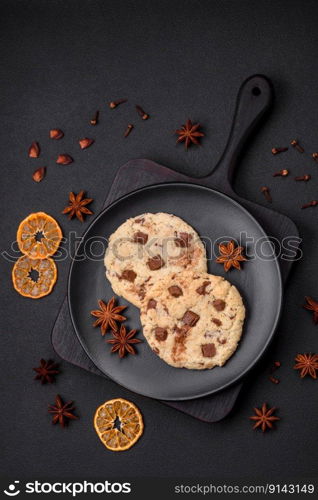 Delicious fresh crispy oatmeal cookies with chocolate and nuts on a black ceramic plate on a dark concrete background