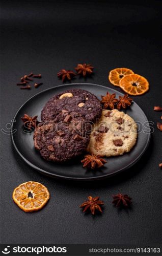 Delicious fresh crispy oatmeal cookies with chocolate and nuts on a black ceramic plate on a dark concrete background