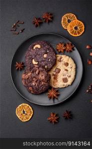 Delicious fresh crispy oatmeal cookies with chocolate and nuts on a black ceramic plate on a dark concrete background