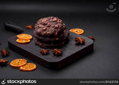 Delicious fresh crispy oatmeal cookies with chocolate and nuts on a black ceramic plate on a dark concrete background