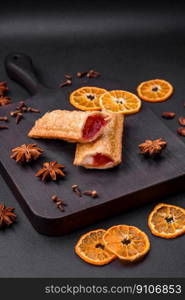 Delicious fresh crispy pie with cherry jam on a wooden cutting board on a dark concrete background